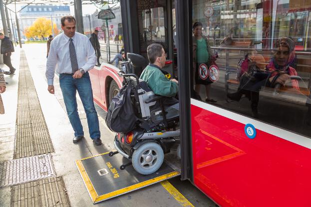 Martin Ladstätter fährt mit seinem Elektrorollstuhl in einen Bus. Daneben steht der Fahrer, bereit, die Rampe einzuklappen.